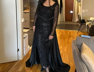 Svart glittrig långklänning med släp - Svart långklänning med glittriga paljetter och transparenta långärmar. Klänningen har ett elegant släp och ett bälte i midjan som ger en snygg siluett. Perfekt för dig som vill sticka ut med en dramatisk look. Storlek 42 men funkar för 40. Pris kan diskuteras