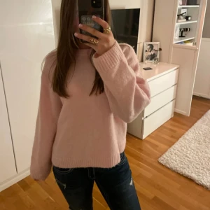 Ljusrosa stickad tröja - Supermysig ljusrosa stickad tröja med rund hals och långa ärmar. Tröjan har en loose passform och breda ribbade muddar vid ärmslut och nederkant. Perfekt för kyliga dagar och enkel att matcha med jeans eller kjol.