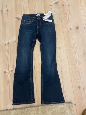 Y2K low bootcut jeans från Gina Tricot - Snygga mörkblå bootcut jeans från Gina Tricot i modellen Y2K low bootcut. Klassisk femficksdesign med dekorativa sömmar och låg midja. Jeansen är tillverkade i jeansmaterial och har coola detaljer som knappar på bakfickorna.        Köpt dom för 599kr och aldrig använt pga att dom är för korta 