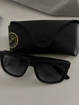 Svarta Ray-Ban  Justin solglasögon - Snygga svarta Ray-Ban Justin solglasögon med klassisk fyrkantig form och polariserade linser. Kommer med original svart fodral och putsduk med Ray-Ban-logga. Köpt för 1800kr så otroligt kap då dem inte är använda. Låda ska finnas och går att leta upp.