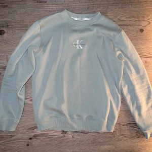 Pastellgrön sweatshirt från Calvin Klein - Säljer en stilren sweatshirt från Calvin Klein i storlek M. Tröjan har rund halsringning, ribbade muddar och en broderad CK-logga på bröstet. Perfekt för en avslappnad och snygg look. Använd 1 gång, så den är som ny. Nypris 850kr.