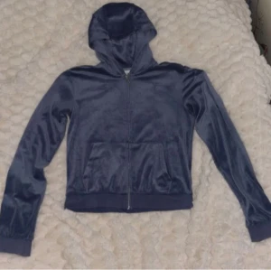 Blå velour hoodie Juicy Couture - Säljer en mörkblå hoodie från Juicy Couture i mjuk velour med dragkedja framtill och huva. Tröjan har långa ärmar, fickor på magen och ett broderat JC-logo på bröstet. Perfekt för chill dagar och snygg att matcha med jeans eller mjukisbyxor. Skriv gärna prisförslag!