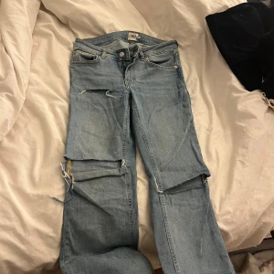 Ljusblå low bootcut jeans från 157 - Ljusblå jeans från 157 med low bootcut-passform. Jeansen har slitna detaljer och stora hål på benen för en edgy look. Klassisk femficksmodell med dragkedja och knapp. Perfekta för dig som gillar en avslappnad och trendig stil.