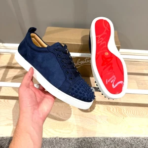 Christian Louboutins - Snygga mörkblå sneakers från Christian Louboutin i mocka med vita sulor och den ikoniska röda undersidan. Skorna har snörning och coola nitar på tån för en edgy vibe. Perfekta för dig som vill sticka ut med exklusiv design och detaljer.