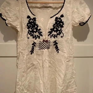 Vit Odd Molly blus - Supersöt vit blus från Odd Molly med svart broderat blommönster framtill, liten rosett och v-ringad hals. Används inte tyvärr då den är superfin. Pris kan diskuteras 💙