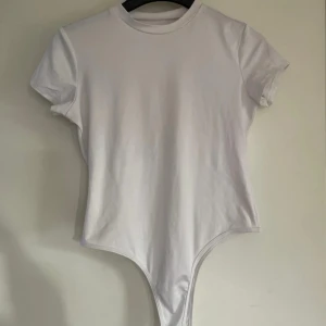 Vit t-shirt body suit - Knappt andvänd och i bra skick. Säljer pga att den är för stor. Det står ingen storlek men skulle gissa på att det är M. Den har två knappar nertill som gör den enkel att stänga! Hör av er vid frågor eller funderingar :)