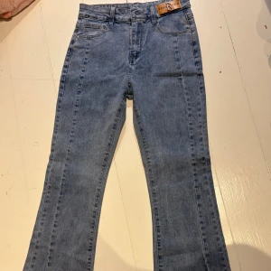 Blå bootcut jeans från Byxha Denim - Snygga ljusblå jeans från Byxha Denim med bootcut passform. Klassisk femficksmodell med tydliga sömmar och slits vid benslutet. Jeansen har en hög midja och är tillverkade i mjukt denimtyg som ger en skön känsla.