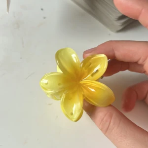 Gul blomformad hårklämma diadem - Säljer en söt hårklämma i form av en blomma i glansig gul plast. Perfekt accessoar för att piffa upp frisyren med en färgklick och unik form. Klämman har starkt grepp och passar både till utsläppt och uppsatt hår.
