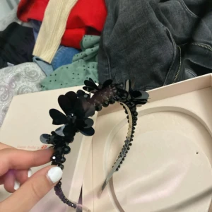 Svart diadem med blommor från H&M - Snyggt svart diadem från H&M dekorerat med stora blommor och glittriga paljetter. Diademet har en metallbas och är täckt av svarta pärlor och plastdetaljer som ger en cool och festlig look. Perfekt accessoar för att lyfta din outfit.