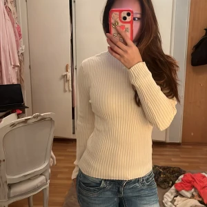 Ribbad polotröja från Zara i beige - Säljer en beige ribbad polotröja från Zara i storlek S. Tröjan har lång ärm, tight passform och hög krage. Materialet är mjukt och stretchigt, perfekt för lager-på-lager. Enkel och stilren design som är lätt att matcha med jeans eller kjol.