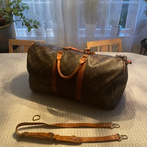 Louis Vuitton Keepall Monogram Resväska 50L - Klassisk Louis Vuitton Keepall resväska i brunt monogrammönster med detaljer i ljust brunt skinn. Väskan har både handtag och avtagbar axelrem i läder. Axelremmens krokar har blivit utbytta och den ena hylsan är av pågrund av att lädret gått sönder. Hylsan finns kvar så den går att laga.                                                                       Ny pris: 21 000 kr