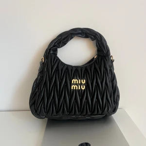 Svart quiltad handväska  - Stilren svart handväska. Väskan har en vadderad handtag och avtagbar axelrem för extra flexibilitet. Perfekt för dig som vill ha en lyxig och trendig accessoar.