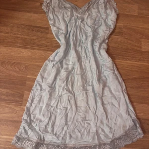 Ljusblå spetsklänning i silke - Superfin ljusblå kortklänning i silkesliknande material med spetsdetaljer vid halsringning och nederkant. Klänningen har v-ringad urringning och är ärmlös, perfekt för en somrig look. Söt och feminin med fina broderade spetskanter. (Defekt syns på tredje bilden, har sytt ärmarna kortare, så resultatet blev lite klumpigt)