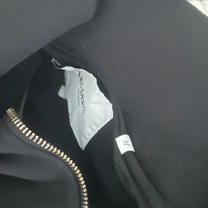 Les deux - Svart kofta från Les Deux med stilren design och silverfärgad dragkedja framtill. Kofta  har hög krage och broderad logga på bröstet. Perfekt för dig som gillar minimalistisk och clean stil. Pris kan diskuteras.