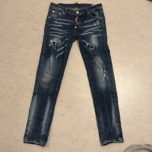Dsquared2 blåa jeans - Snygga blå jeans från Dsquared2 med slitningar och hål på benen för en edgy look. Jeansen har skinny passform, klassisk femficksdesign och tydliga slitdetaljer framtill och baktill. Perfekta för dig som gillar streetstyle och vill sticka ut.