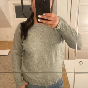 Grå stickad tröja från ONLY - Mysig grå stickad tröja från ONLY i storlek M. Tröjan har rund hals, ribbade muddar vid ärmslut och nederkant samt långärmad passform. Perfekt för dig som gillar enkel och clean stil. Snygg att matcha med jeans eller kjol.