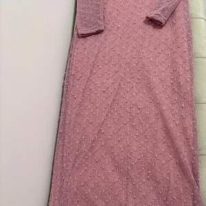 Rosa stickad långklänning med struktur - Säljer en rosa långklänning med stickad struktur och diskreta bollar i mönstret. Klänningen har långa ärmar och är fodrad med mjukt tyg på insidan för extra komfort. Perfekt för dig som gillar unika detaljer och en mysig känsla.