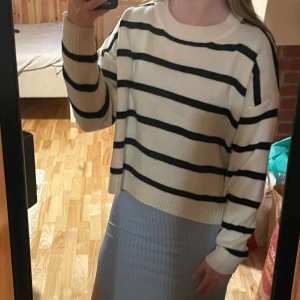 Randig stickad tröja i vitt och svart - Snygg stickad tröja med breda svarta ränder på vit botten. Modellen är loose fit med rund hals och långa ärmar. Perfekt för dig som gillar en chill och trendig stil. Ribbstickade muddar vid ärmslut och nederkant ger extra detalj.