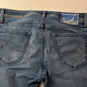Blå jeans från Jacob Cohen - Snygga blå jeans från Jacob Cohen med klassisk femficksdesign, ljus tvätt och kontrastsömmar. Jeansen har raka ben och knappgylf, samt en broderad J på myntfickan och patch bak i blått. Perfekta för en avslappnad och stilren look.