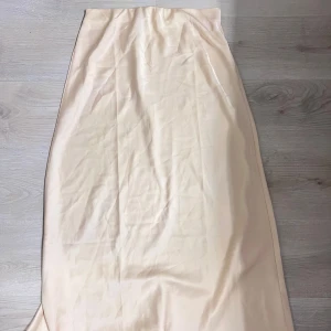 Ljusbeige långkjol i satin - Ljusbeige långkjol med mjuk satinfinish. Kjolen har en rak och enkel siluett form som är jätte fin på