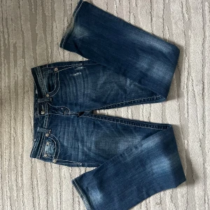 Miss Me bootcut jeans med broderi - Snygga blå bootcut jeans från Miss Me med kontrastsömmar och broderade bakfickor med korsdetaljer. Jeansen har klassisk femficksdesign, silverfärgade knappar och coola slitningar. Perfekta för dig som vill sticka ut med detaljer och unik stil. Jeansen är i storlek 27 men jag skulle säga att de sitter som en 36. Jeansen är köpta secondhand i london på camden market då ordinarie pris var 1500 kr. Jeansen är superbra i längden och har bara några få slitningar längst ner. 