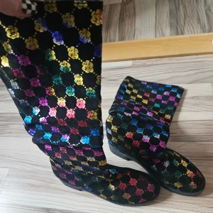 Svarta stövlar med regnbågsrosor - Unika svarta stövlar med färgglatt blommönster i regnbågens alla färger. Skorna har platt sula och är tillverkade i ett mjukt material med glittriga rosor i gult, blått, rosa, lila, grönt och rött. Perfekta för dig som vill sticka ut med din stil. Endast använda inomhus 1 gång. 