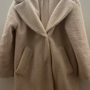 Beige teddyjacka från H&M XS - Säljer en beige teddyjacka från H&M i storlek XS. Jackan har bred krage, två stora fickor och stängs med tryckknappar. Materialet är mjukt och fluffigt, perfekt för kalla dagar. Fodrad insida för extra komfort och värme.