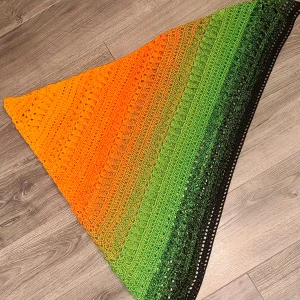 Färgglad virkad triangelsjal - Handvirkad triangelsjal i snygg färgskiftning från orange till grönt och svart. Virkat med Halloween Dahlia i 100% bomullsgarn. Sjalen har ett luftigt mönster med hål och detaljerade virkade partier. Pris är för material + tidsfördriv.