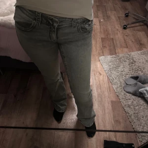 Grå bootcut jeans med fickdetaljer - Säljer ett par grå jeans från Ginatricot med bootcut passform och snygga fickor med knappdetaljer bak. Jeansen har normal midja och är tillverkade i klassiskt denimtyg. Perfekt för dig som gillar en chill och trendig look.