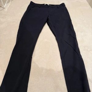 Svarta kostymbyxor från Dondup - Snygga svarta kostymbyxor från Dondup, tillverkade i Italien. Byxorna har raka ben, bälteshällor och två bakfickor med knappar samt en liten metall-logga. De är i mycket bra skick och är i strl 32.