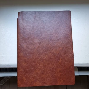 Anteckningsbok läderbunden - Stilren anteckningsbok med brunt läder.. Perfekt för att skriva dagliga tankar, planera veckan eller samla viktiga adresser och telefonnummer. Innehåller även praktiska sidor med internationella koder och väderstatistik. Passar dig som vill hålla ordning på livet med stil. Rivit ut två sidor, annars felfri