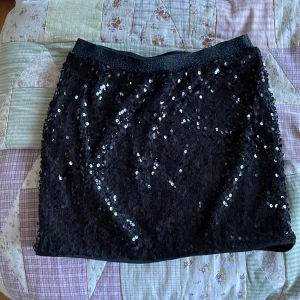 Svart paljettkjol från Lindex - Svart kortkjol från Lindex med glittrande paljetter över hela ytan och ett elastiskt midjeband. 