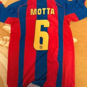 FC Barcelona Motta #6 Nike fotbollströja - Säljer en klassisk FC Barcelona fotbollströja från Nike med Motta och nummer 6 på ryggen. Tröjan har breda blå och röda ränder, klubbmärke på bröstet och gul Nike-logga. Tillverkad i lätt och ventilerande material, perfekt för match eller träning.