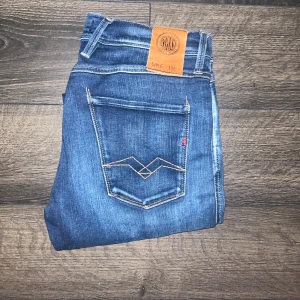 Replay Anbass Hyperflex jeans - Snygga Replay Anbass Hyperflex jeans i klassisk blå färg med coola kontrastsömmar och broderade bakfickor. Slimmad passform och stretchigt material för extra komfort. Midja 38cm, längd 101cm. JAG SKICKAR EJ FLER BILDER NÄR JAG BÄR JEANSEN! för storleksguide hänvisar jag till måtten och för bättre inblick i passformen rekommenderar jag att googla på modellnamnet. Jeansen kan vara uppsydda utan att jag noterat det så kolla måtten noggrant :) 32