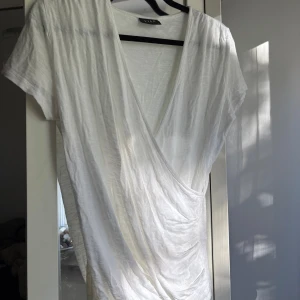 Vit omlottopp från Vila XS - Säljer en vit omlottopp från Vila i storlek XS. Toppen har korta ärmar, djup v-ringning och en snygg omlottdesign framtill. 