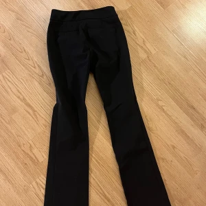 Svarta kostymbyxor från Ann Taylor - Snygga svarta kostymbyxor från Ann Taylor i klassisk rak modell. Byxorna har en stilren design med diskreta fickor och är tillverkade i ett mjukt, följsamt material som ger en dressad look. Perfekta för dig som gillar en clean och tidlös stil.