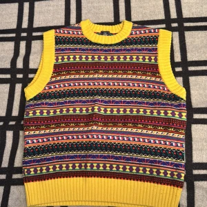 Färgglad stickad väst från J.Press - Säljer en stickad väst från J.Press med galet färgglada ränder och mönster i gult, blått, rött, grönt och svart. Västen har ribbade kanter i klar gul och är gjord i 100% bomull. Perfekt för dig som vill sticka ut med en unik och retro vibe.