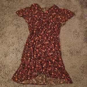Röd blommig kortklänning S - Söt röd kortklänning med blommigt mönster och volangkant. Klänningen har korta ärmar och en mjuk, flowy passform som ger en avslappnad vibe. Perfekt för dig som gillar färg och mönster. Materialet känns lätt och bekvämt mot huden.