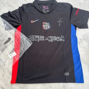 FC Barcelona x Nike fotbollströja S - FC Barcelona x Nike fotbollströja i svart med röda och blå sidopaneler. Tryck med Travis Scott Cactus Jack och UNHCR-logga. Kortärmad modell i lätt Dri-Fit polyester, klubbmärke på bröstet och grafiska detaljer framtill.