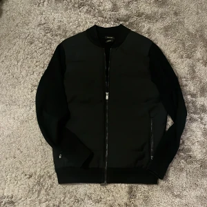 Svart Cardigan från Massimo Dutti - Stillig svart cardigan från Massimo Dutti. Jackan har dragkedja framtill och två fickor. Den är storlek M och är nästan helt ny förutom att Massimo Dutti lappen inuti jackan har lossnat på ena sidan.