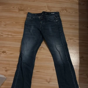 Replay blue jeans  - Snygga blå jeans från Replay med klassisk femficksdesign. Jeansen har slitningar och tvättade detaljer för en cool look. Märkespatch i läder baktill i midjan. Perfekta för dig som gillar en avslappnad men stilren stil.