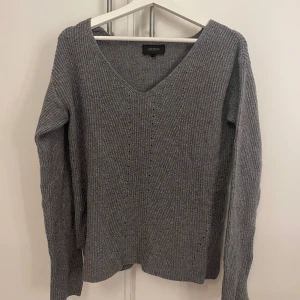 Grå stickad tröja med v-ringning - Mysig grå stickad tröja från Alice Bizous i storlek S. Tröjan har en snygg v-ringad hals och ribbad struktur som ger en cool och avslappnad vibe. Perfekt för att hålla sig varm under höst och vinter. Långärmad och passar till många olika stilar.