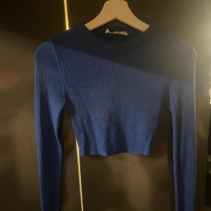 Blå ribbad croppad långärmad topp - Säljer en blå croppad topp med lång ärm och ribbad struktur. Toppen har en rund halsringning och är figurnära i modellen, perfekt att styla med höga jeans eller kjol. Materialet är stretchigt och bekvämt.