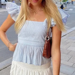 Ljusblå blus med volangärmar och knyt - Supersöt ljusblå blus med fyrkantig urringning, volangärmar och knyt i ryggen. Toppen har en lätt rynkad struktur. Perfekt för sommarens alla häng!