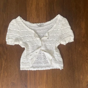 Vit stickad blus från Amisu - Supersöt vit stickad blus från Amisu med korta ärmar och rund hals. Blusen har ett ribbat mönster med små hål och knappar. Stickad i mjukt material för extra komfort. 