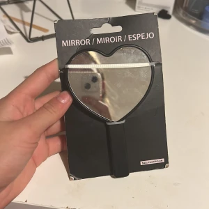 Hjärtspegel med strass - Snygg handhållen spegel i hjärtformad design med glittrande strass på baksidan. Perfekt för sminkning eller touch-ups. Storlek 12,5 x 8,5 cm. Förpackningen är något sliten men spegeln är i nyskick. Saknar lite kristaller.