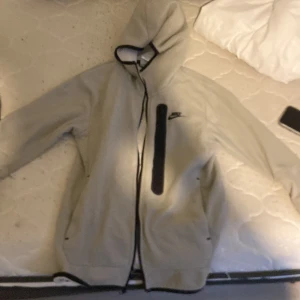 Grå Nike hoodie med dragkedja - Säljer limeted edition en grå hoodie från Nike med hel dragkedja och svart detalj på bröstet. Tröjan har huva med snörning och långa ärmar. Perfekt för dig som gillar sportig och avslappnad stil.