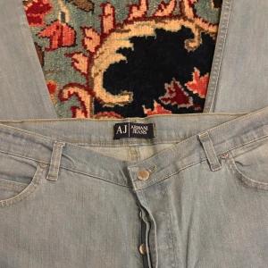 Ljusblåa Armani Jeans classic fit - Snygga ljusblåa jeans från Armani Jeans i klassisk rak modell. Byxorna är tillverkade i 100% bomull och har fem fickor, knappgylf och ikonisk AJ-logga på bakfickan. Perfekta för dig som gillar en clean och tidlös look.