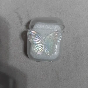 AirPods 1/2 Skal Fjäril Transparent - Stilrent transparent skal till AirPods 1/2 med dekorativ fjäril. Ger bra skydd mot repor och stötar. Skalet är i nyskick utan synligt slitage. Perfekt för dig som vill ge dina AirPods ett unikt och personligt utseende. Jag säljer den för att jag råkade köpa för liten