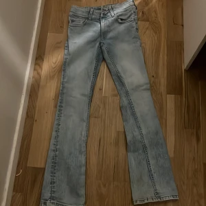 Ljusblå bootcut jeans från H&M - Säljer ett par ljusblå bootcut jeans från H&M med låg midja och justerbar midja. Jeansen har klassisk femficksdesign och är tillverkade i denim med snygg tvättad look. Perfekta för dig som gillar retrovibbar och bekväm passform. (Kan vara som en liten 158) rekommenderas ej till folk över 160 
